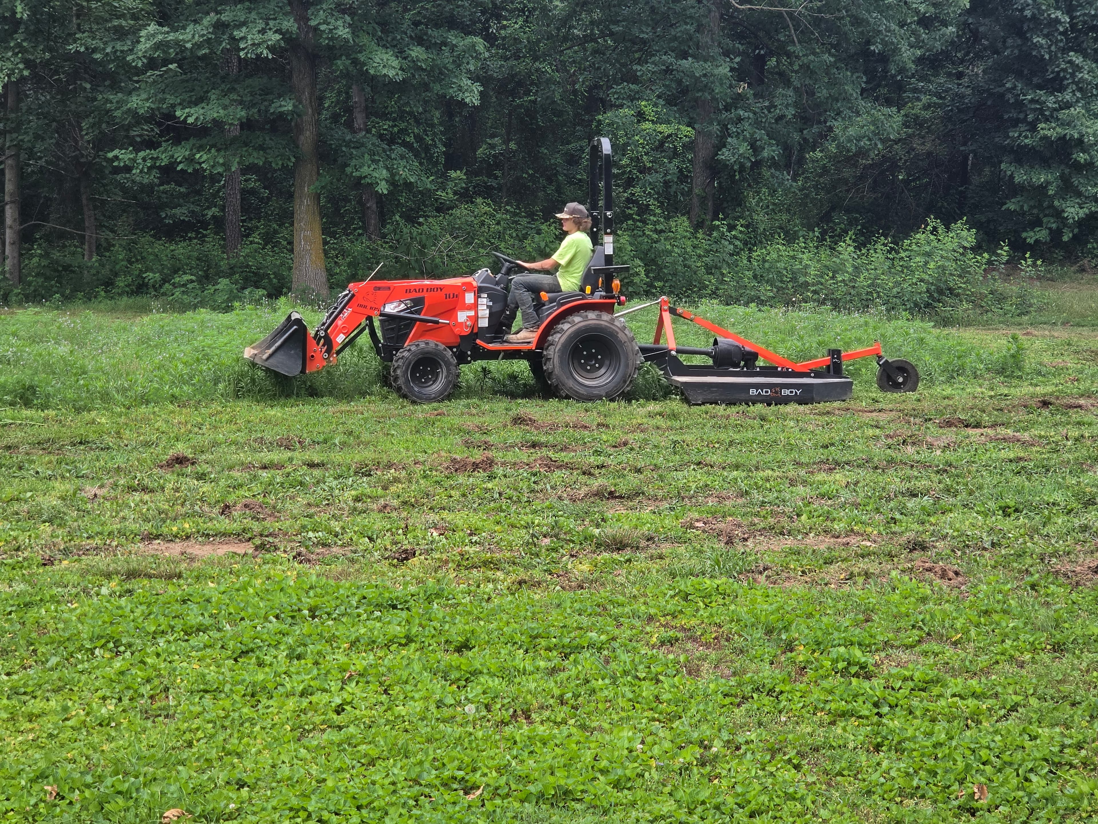 Compact tractor with a rotary cutter clearing a heavily overgrown field